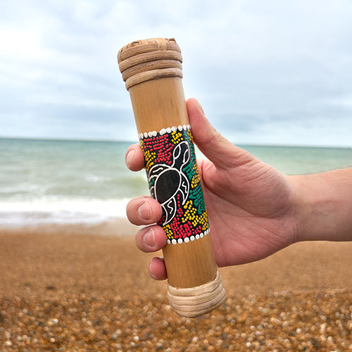 Hand holding a decorated bamboo rainstick with a beach background