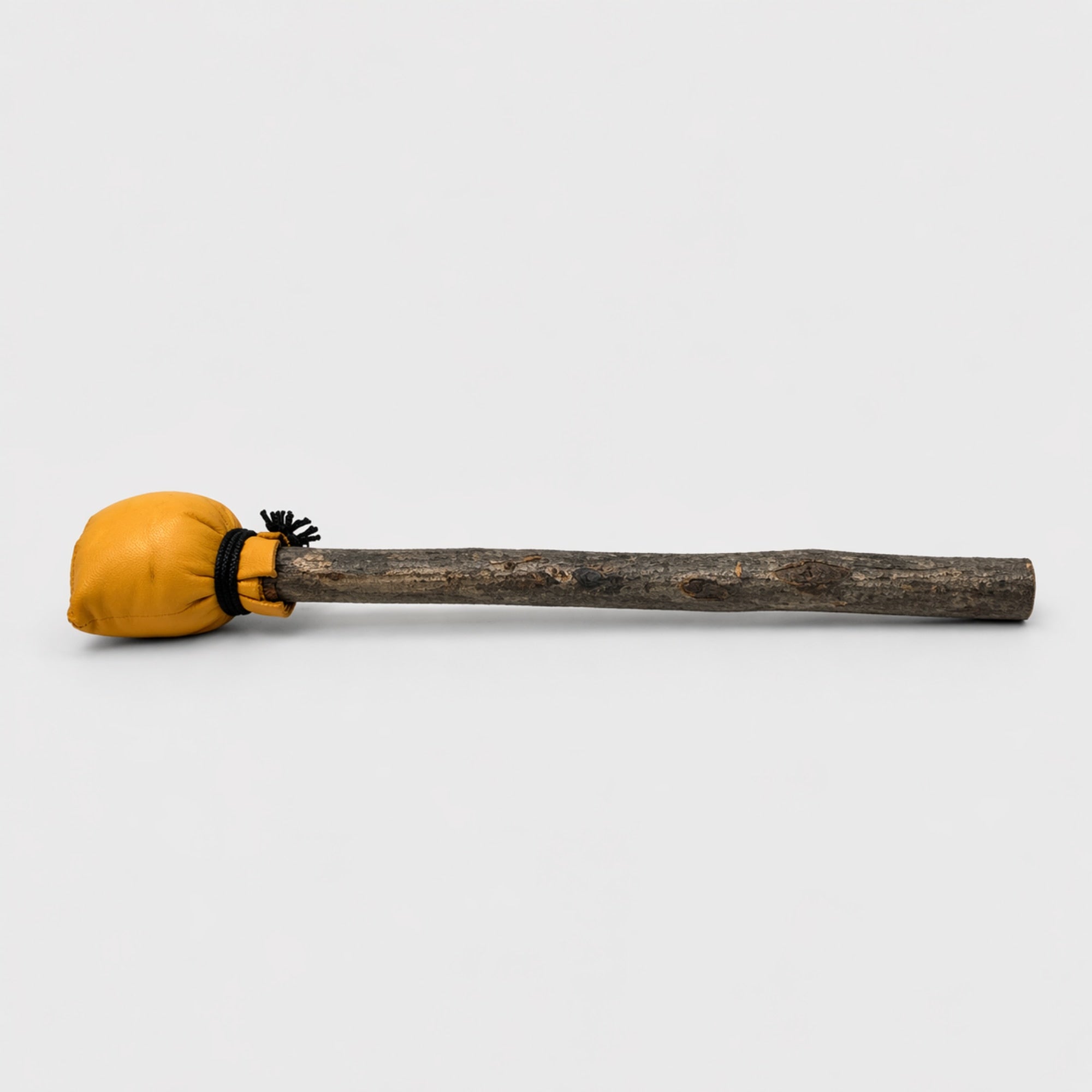 Yellow shamanic drum beater with natural wooden handle on a light grey studio background